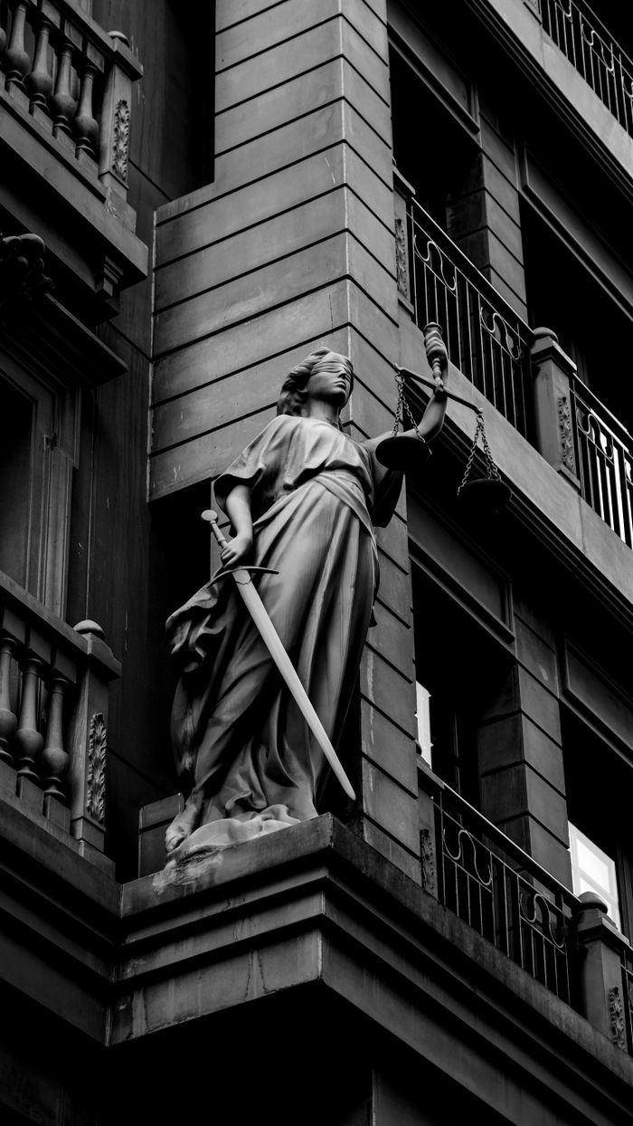 Services A dramatic black and white photo of a justice statue holding a sword and scales.