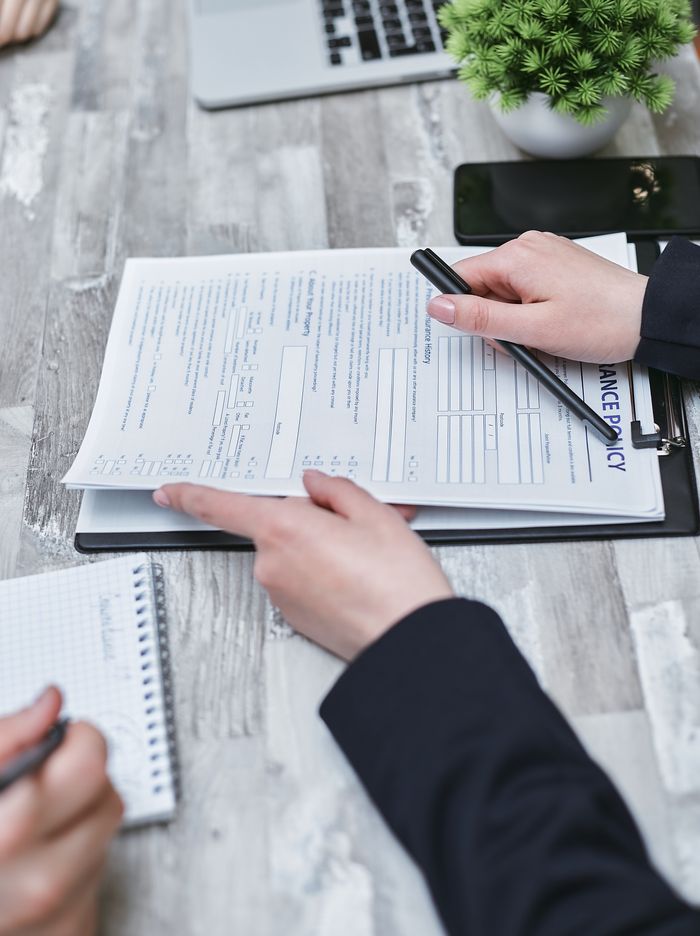 Services Close-up of hands analyzing insurance policy paperwork with pen on table.
