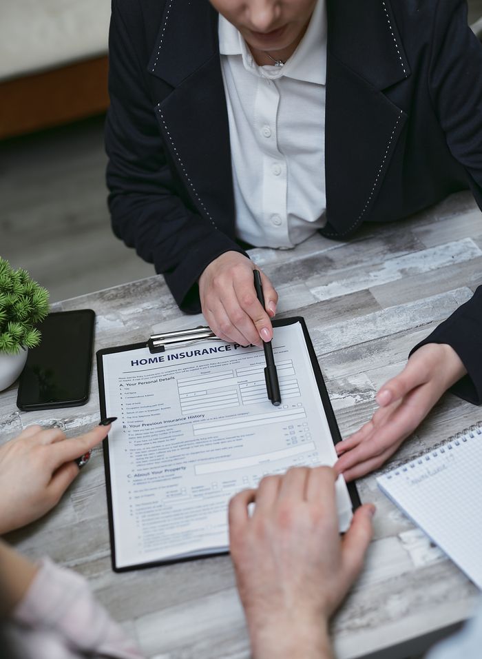 Services An agent and clients discussing paperwork for home insurance at a meeting table.