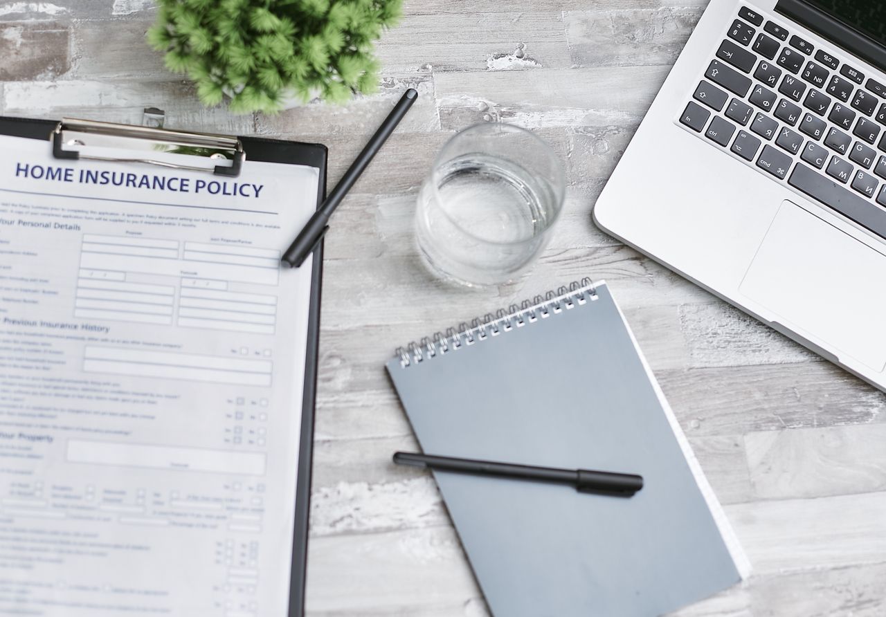 Services Flat lay of a workspace with a home insurance policy, laptop, and notebook on a desk.
