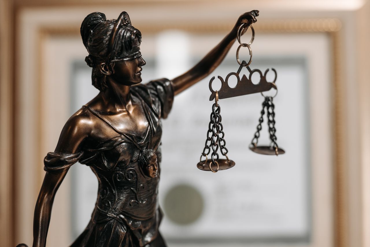 Services Close-up of a bronze Lady Justice statue holding scales in an office environment.